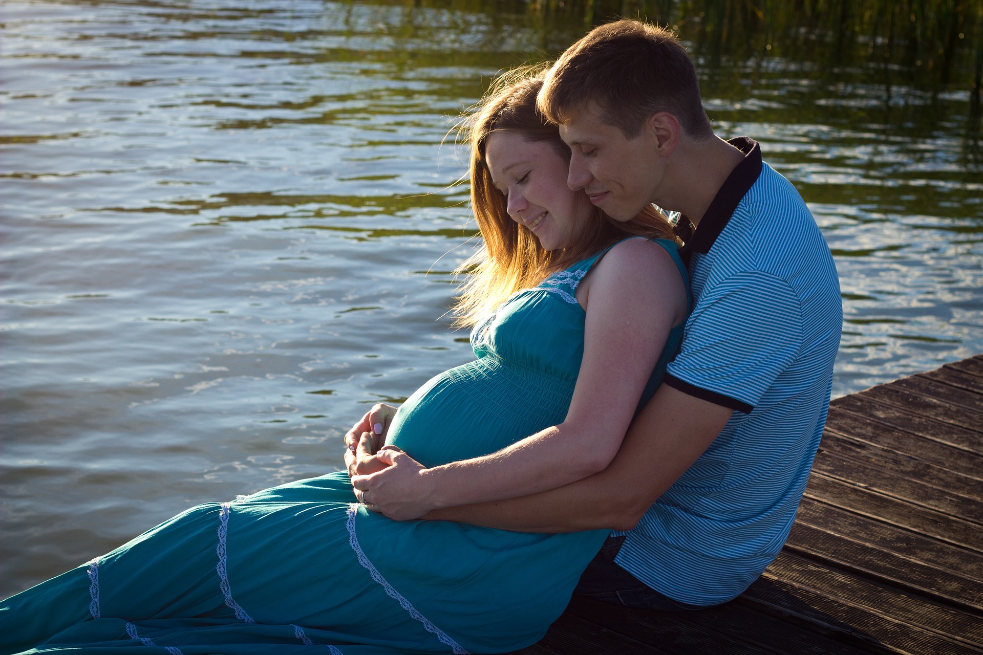 Schwangeres Pärchen sitzt glücklich am See